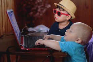 a baby and a child with glasses pretending to build a website on a laptop.