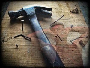 Hammer with bent nails in wood board. man in anguish holding his head.